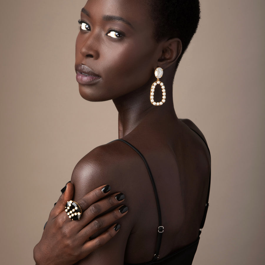 Woman wearing large earrings and a ring against a neutral background