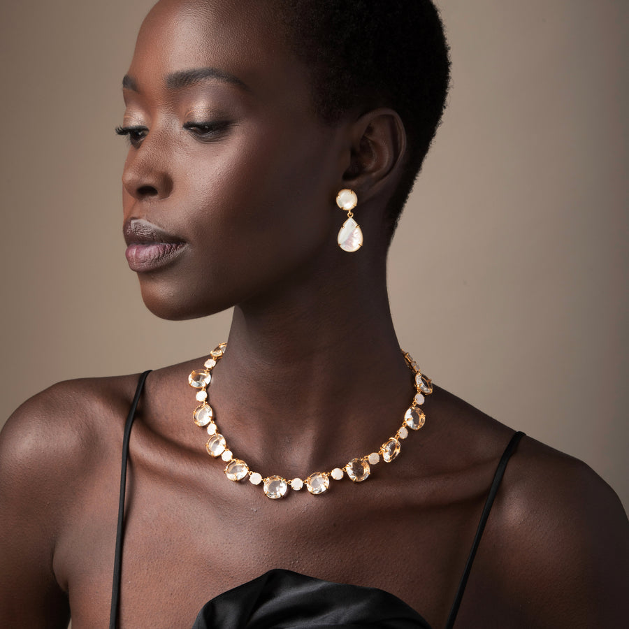 Woman wearing a gold necklace and earrings against a neutral background
