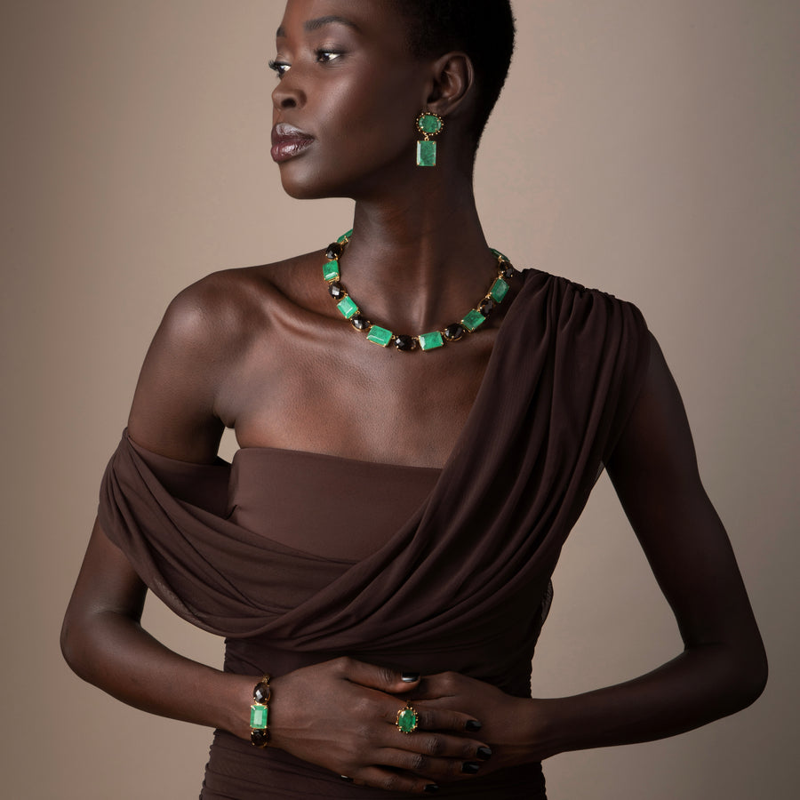 Woman wearing a brown dress and green jewelry against a beige background