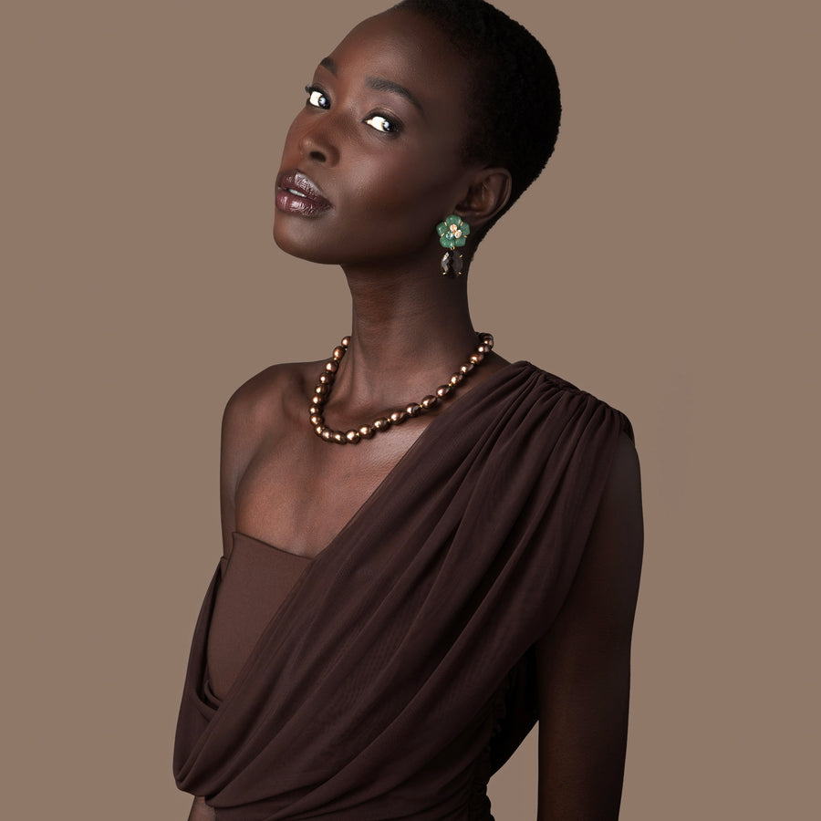 Woman wearing a brown dress and necklace against a beige background