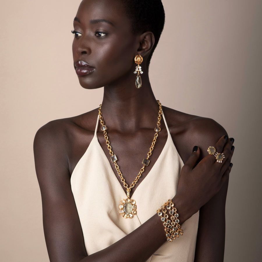 Model wearing Bounkit Juniper Earrings with crystal clusters and teardrop stone, styled with matching gold chain necklace, gemstone bracelet, and statement ring.