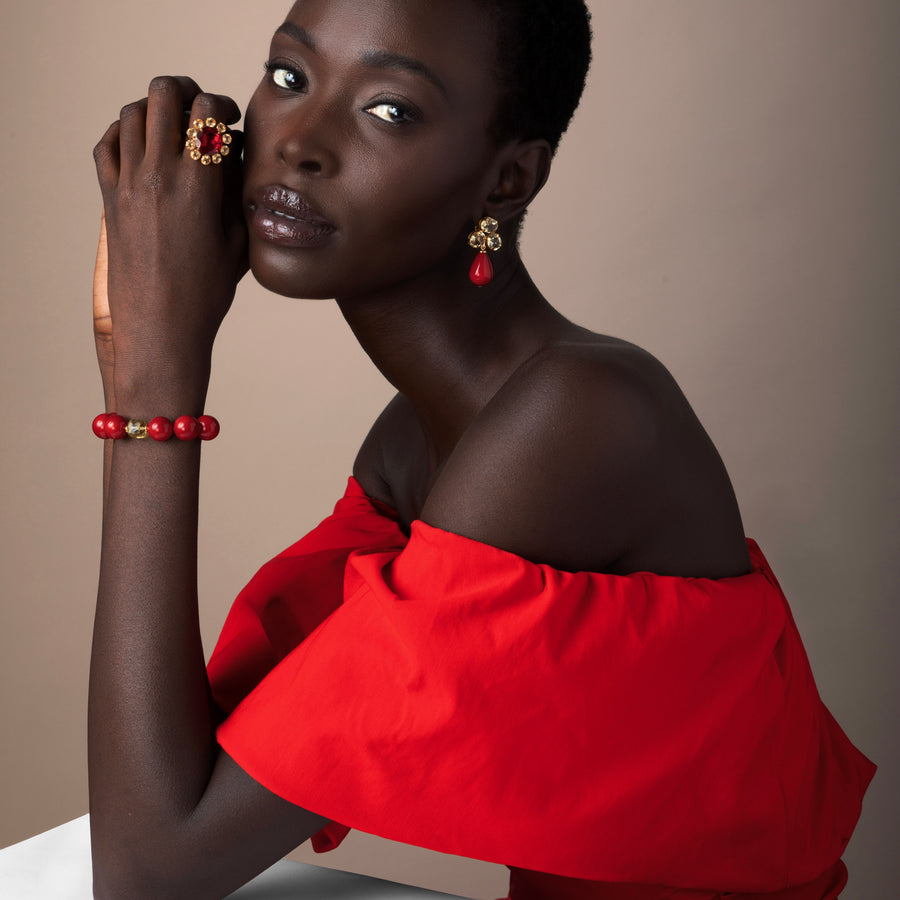 Woman wearing a red off-shoulder top with jewelry against a neutral background