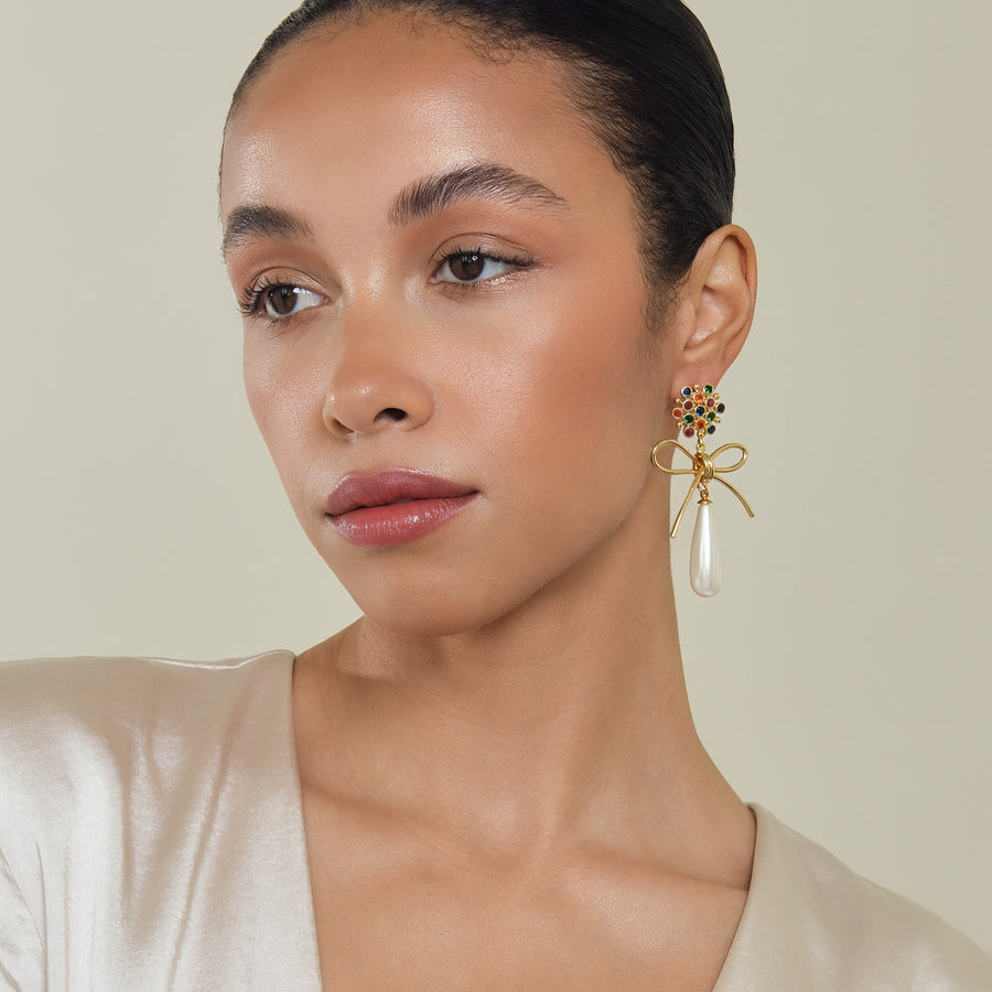 Model wearing convertible Bounkit earrings with a colorful cluster of stones, golden bow, and pearl drop, styled with a sleek updo and satin top.