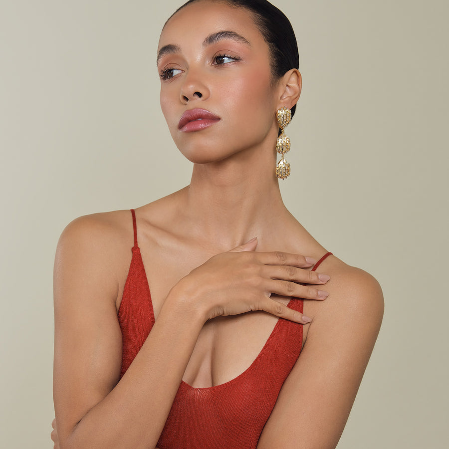 Woman wearing a red top and gold earrings against a beige background