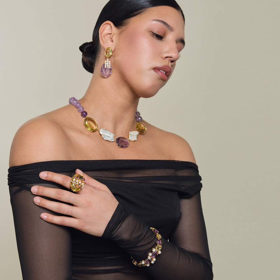 Woman wearing a colorful necklace, ring, and earrings against a neutral background