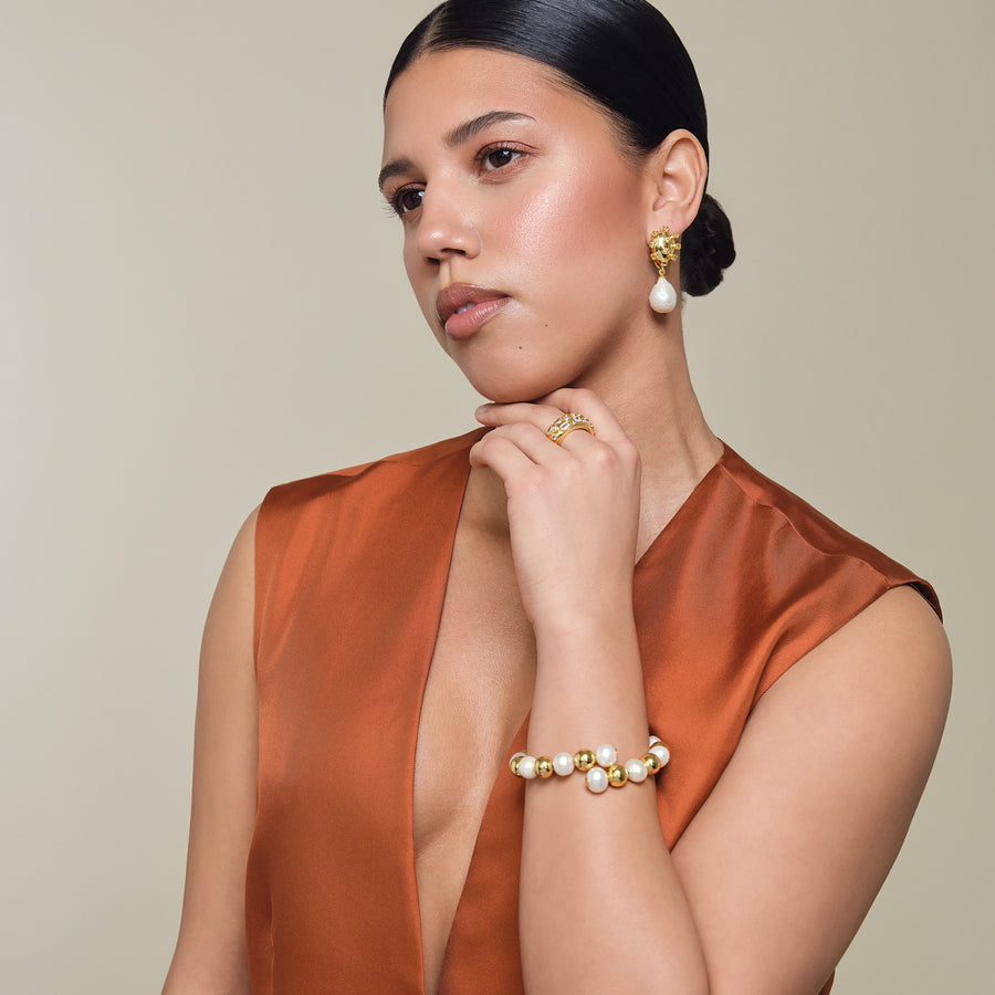 Woman wearing gold and pearl jewelry against a neutral background